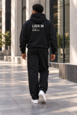 Back view of a black hoodie with LOCK IN, a thin divider, and QUIETLY above plain black sweatpants